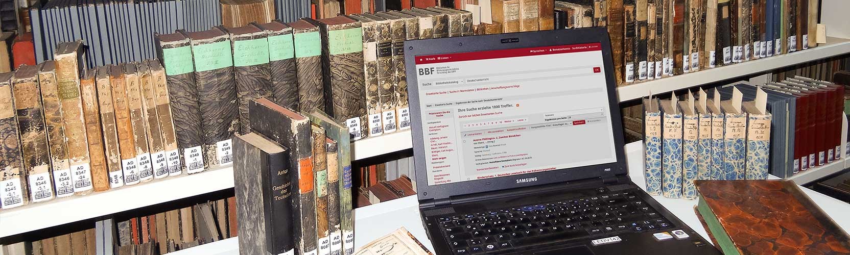 Schmuckbild: Laptop auf einem Tisch mit historischen Büchern im Hintergrund